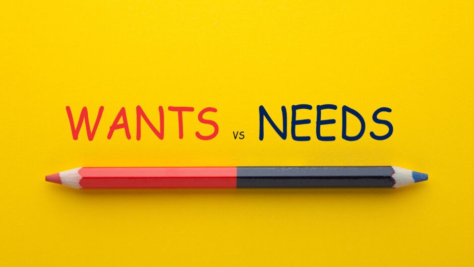 この画像は黄色い背景に赤と青の鉛筆が写っている写真です。鉛筆の上には、赤と青の大文字で「WANTS vs NEEDS」と書かれています。鉛筆は赤い鉛筆が「WANTS」の単語を指し、青い鉛筆が「NEEDS」の単語を指しているように配置されています。